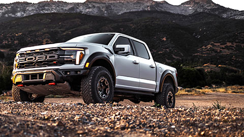 Ασημί off-road pickup σε βραχώδες έδαφος με βουνά στο φόντο.