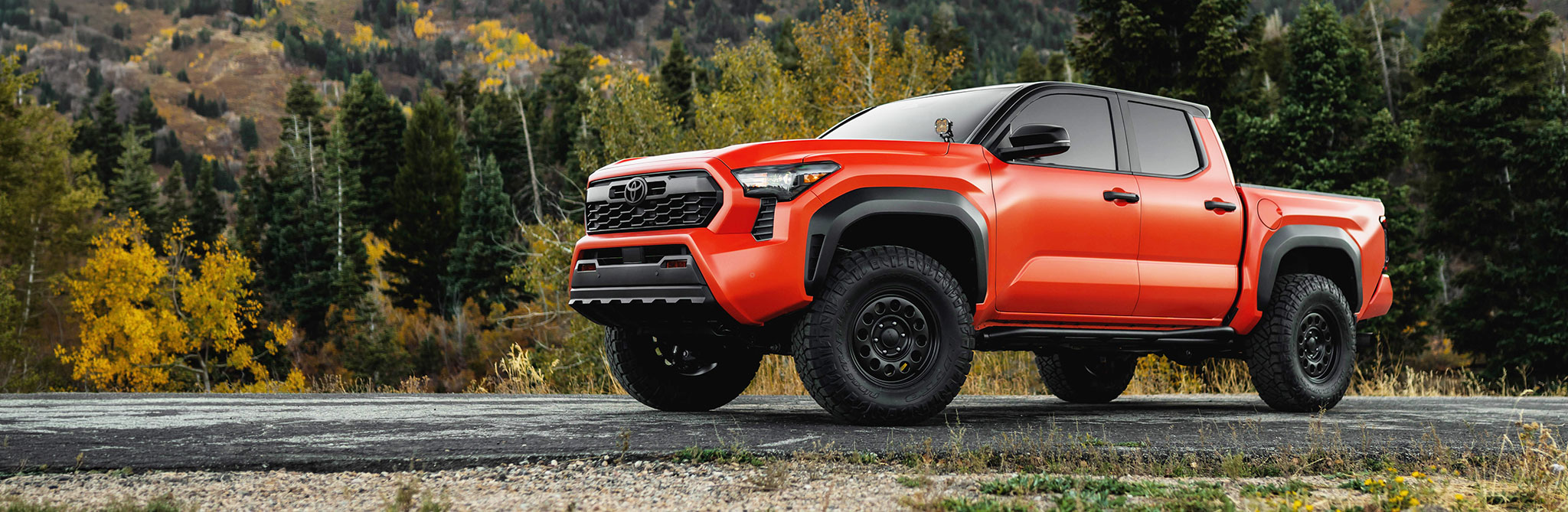 Πορτοκαλί αυτοκίνητο off-road σε χωματόδρομο με φόντο πυκνά δέντρα και βουνά.